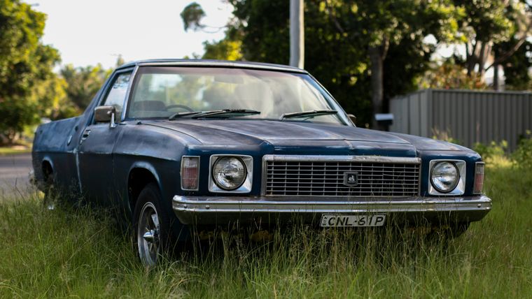 Unrestored, patina Holden HQ-series ute parked in long grass.