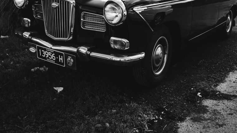 Black-and-white photo of a classic black sedan parked beside a chain-link fence