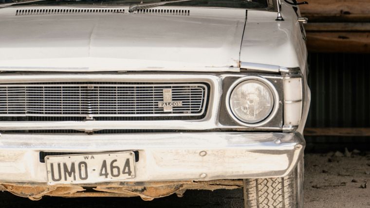 The front of a white Ford Falcon parked inside a corrugated iron shed, still wearing its Western Australian numberplate.