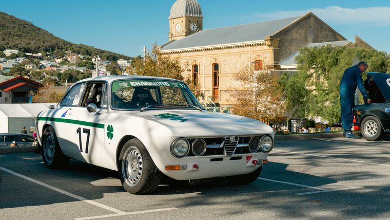 White Alfa Romeo GTV with racing number 17 parked in a historic town square