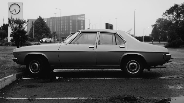 Black and white photograph of a Holden Kingswood sedan parked alone in an empty city car park, seen side-on.