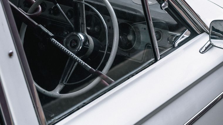 Driver's side window, chrome frame and steering wheel of a restored white 1960s sedan